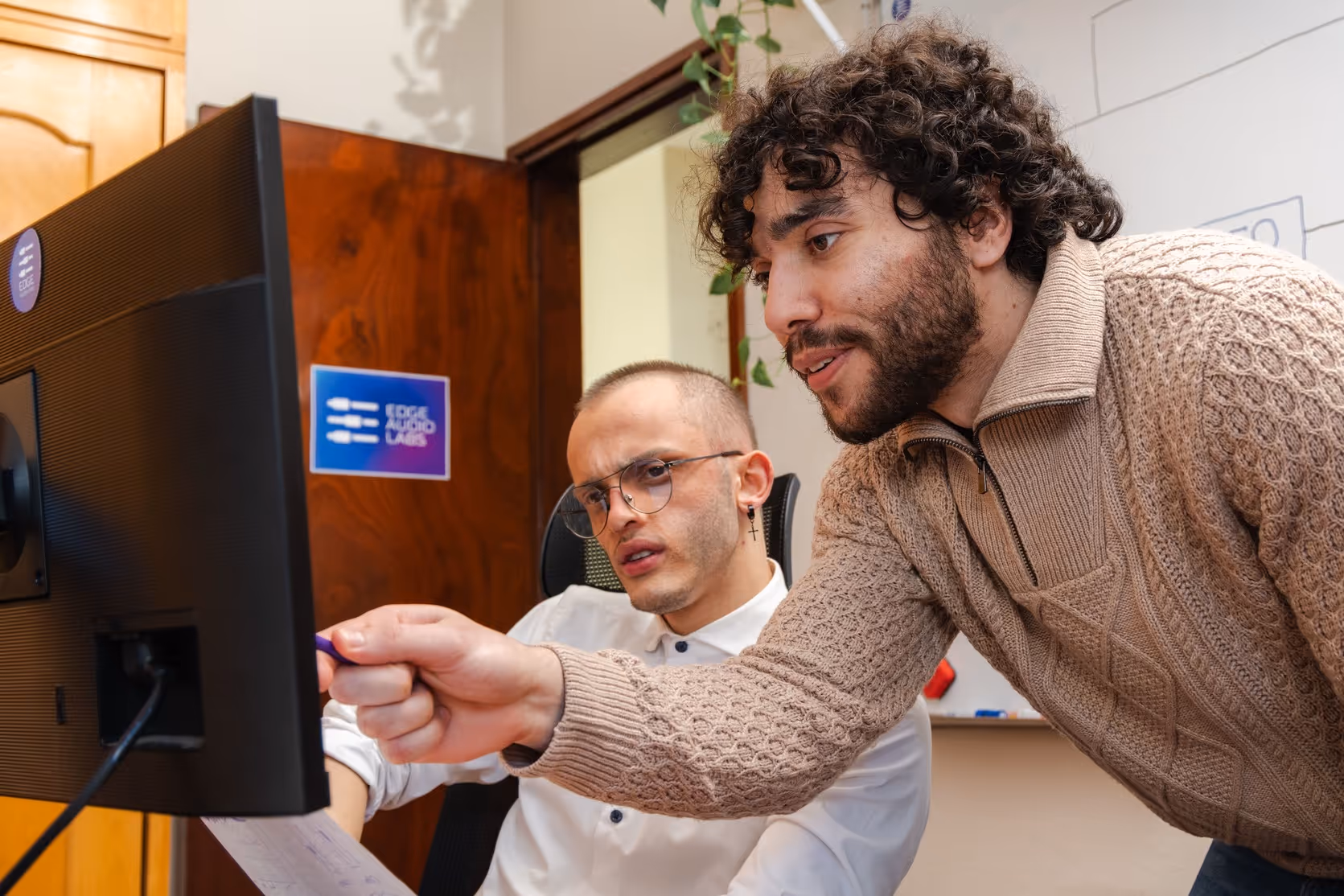 Team members from Edge Audio Labs collaborating on a project in the office, focused on a computer screen while discussing audio technology solutions.