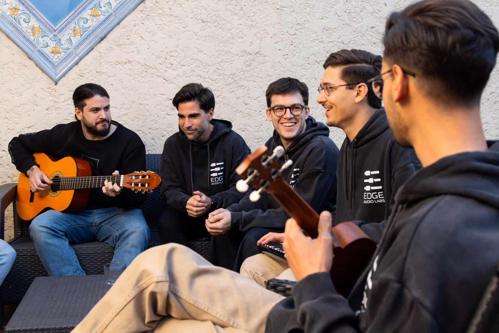 Members of the Edge Audio Labs team sharing a relaxed moment outdoors, playing guitar and ukulele together while wearing company hoodies and enjoying a casual conversation.